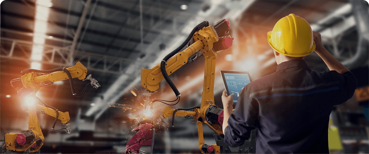 An image of a worker in a yellow hard hat standing in a factory setting, looking towards a large yellow robotic machine. This industrial scene is used to represent the institutional-level precision and technical solutions of the cash management services.