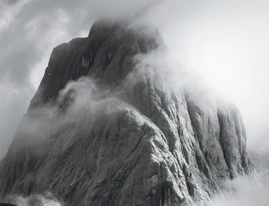 Black and white photo of a fog-shrouded mountain peak rising above clouds, evoking the long game of extending corporate cash maturities.